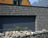 Nowoczesna brama garażowa otoczona gabionami wypełnionymi kamieniem. Co to za kamień? To trwały i estetyczny element architektury.