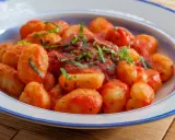 Pyszne gnocchi w sosie pomidorowym, posypane świeżą bazylią, podane w niebiesko-białej misce.