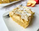 Ein Stück saftiger Apfelkuchen mit Apfelmus, bestreut mit Puderzucker und Mandelblättchen, wartet auf dem Teller.