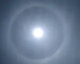 Jasne niebo z widocznym słońcem otoczonym tęczowym kręgiem. To piękny efekt halo.