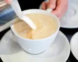 Milch wird in eine Tasse mit Kaffee gegossen, um ein cremiges Café au Lait zu kreieren.