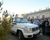 Papież Franciszek, mimo swojego vatican wiek, pozdrawia wiernych z białego mercedesa. Tłum wiwatuje, a niektórzy robią zdjęcia.