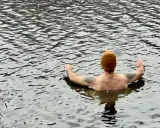 Man med orange mössa och tatueringar njuter av kallt bad i en sjö.