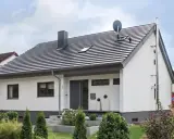 Nowoczesny dom z białymi ścianami i szarym dachem o kącie nachylenia dachu 30 stopni. Na dachu komin, anteny i okna dachowe.