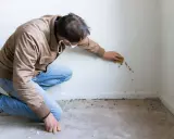 Hombre con mascarilla limpiando manchas de humedad de la pared con una esponja.