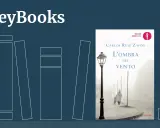 Copertina del libro "L'ombra del vento" di Carlos Ruiz Zafón, con un'immagine suggestiva di una strada nebbiosa e due figure.