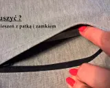 Szara tkanina z widocznym zamkiem i patką. Dłoń z czerwonym lakierem do paznokci wsuwa się do kieszeni z patką.