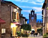 Serata magica al castello di Gradara. Vicoli illuminati, torre dell'orologio e gente che passeggia.