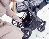 Kobieta wkłada coś do kosza wózka Cybex Priam. Waga wózka jest niewielka, co ułatwia manewrowanie w śniegu.