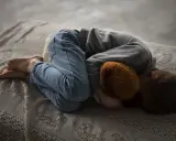 Un niño abraza un peluche, acurrucado en una cama. Una imagen que evoca la necesidad de saber como explicar la muerte a un niño.