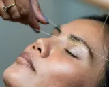 Une main experte réalise un rehaussement sourcils avec du fil. La précision du geste promet un regard sublimé.