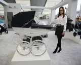 Elegancka kobieta prezentuje najdroższe wózki dziecięce, w tym luksusowy model Silver Cross z białym koszem i czarną gondolą.