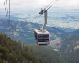 Kolejka gondolowa nad lasem i doliną z widocznym miastem w tle.