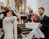 Para młoda wypuszcza gołębie na kameralnym weselu. W tle widać gości z telefonami.