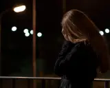 Kobieta z rudymi włosami, zakrywająca twarz dłońmi, stoi na balkonie nocą. W tle migoczą światła uliczne, symbolizujące stres przed seksem.