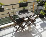 Un piccolo tavolo e sedie in legno su un balcone, con piante e lucine, perfetti per trasformare il balcone in terrazzo.