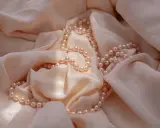 Un filo di perle rosa pallido adagiato su una morbida seta color crema. Un'idea perfetta per regalare perle.