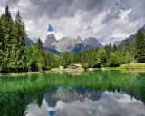 Riflessi perfetti sul lago Welsperg, con montagne maestose e una baita accogliente tra gli alberi.