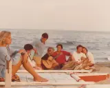 Giovani su una spiaggia, un gruppo di amici che ricorda i film estivi italiani, con chitarra e falò.