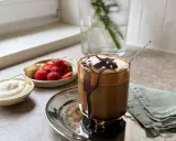 En läcker frappe med chokladsås och grädde, serverad med färska jordgubbar och en bit bakverk. Ett perfekt frappe recept för en solig dag.