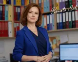 Kobieta w niebieskiej marynarce stoi przed regałami z segregatorami.