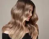 Mujer con cabello largo y ondulado, con un degradado de castaño a rubio. Un ejemplo de cómo aclarar el pelo teñido para un look natural.