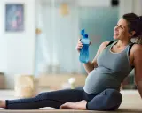 Donna incinta sorride con una bottiglia d'acqua dopo una sessione di yoga in gravidanza.