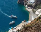Barche turistiche navigano nel blu intenso del porto di Santorini, con le case bianche aggrappate alla scogliera.