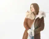Mujer con abrigo de pelo natural en la nieve, lista para limpiar su ropa de invierno.