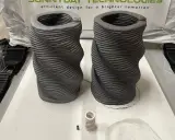 Dos jarrones retorcidos creados mediante impresión 3D hormigón. Se aprecian las capas de material.