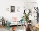 En avslappnad inredning hemma med vit soffa, konst på väggen, en basketboll och en skateboard. En stor klocka hänger på ett metallgaller.