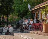 Folk njuter av solen på uteserveringar i Stockholm. En glasskylt syns ovanför en servering.