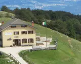 Il rifugio Posa Puner, con la bandiera italiana che sventola, domina un paesaggio montano verdeggiante.