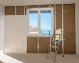 Instalación de un trasdosado de pladur con aislamiento, mostrando la estructura metálica, la lana de roca y una placa de yeso.