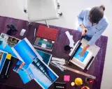 Kobieta przycina wydruki wykonane techniką druk lateksowy. Na stole leżą zdjęcia, laptop i aparat.