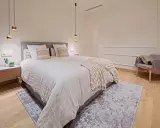 Dormitorios relajantes con cama amplia, manta texturizada, sillón acogedor y luces colgantes.