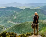 Mann mit Kamera genießt die Aussicht auf kurvige Straße in grünen Bergen. Perfektes Ziel für Wandern in Spanien.