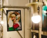 Plakat z kobietą w beżowym płaszczu i zielonym swetrze, trzymającą czerwoną torebkę. Stylizacja przypomina modę z **Pezet Tokyo**.