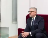 Mężczyzna w garniturze i okularach siedzi na czerwonym fotelu.