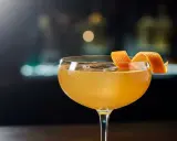 En gyllene cocktail i ett coupeglas, garnerad med en apelsinzest. Ett klassiskt, old fashioned recept som lockar.