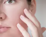 Dita accarezzano delicatamente il viso, mostrando una pelle reattiva e sensibile, bisognosa di cure delicate.