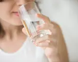 Kobieta w ciąży gasi pragnienie, pijąc wodę ze szklanki.