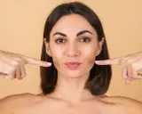 Doigts pointés vers les joues, une femme montre comment repulper son visage pour un look plus jeune et plein.