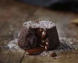 Un fondant au chocolat dégouline de sa ganache onctueuse sur une planche en bois rustique, saupoudré de sucre glace.