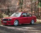 Czerwone bmw e30 coupe z białymi felgami na tle jesiennego lasu.