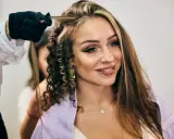 Fryzjerka tworzy loki na włosach kobiety z wyraźnymi, chunky highlights.