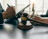 Młotek sędziowski na stole, obok dłonie prawników pracujących na tabletach.