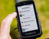 Palec dotyka ekranu Hammerhead Karoo 3, wyświetlającego listę rozszerzeń, w tym Epic Ride Weather i GiBLi.