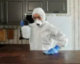 Osoba w kombinezonie ochronnym dezynfekuje blat kuchenny.