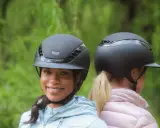Zwei Reiterinnen mit schwarzen Reithelmen, bereit für einen Testritt im Grünen.